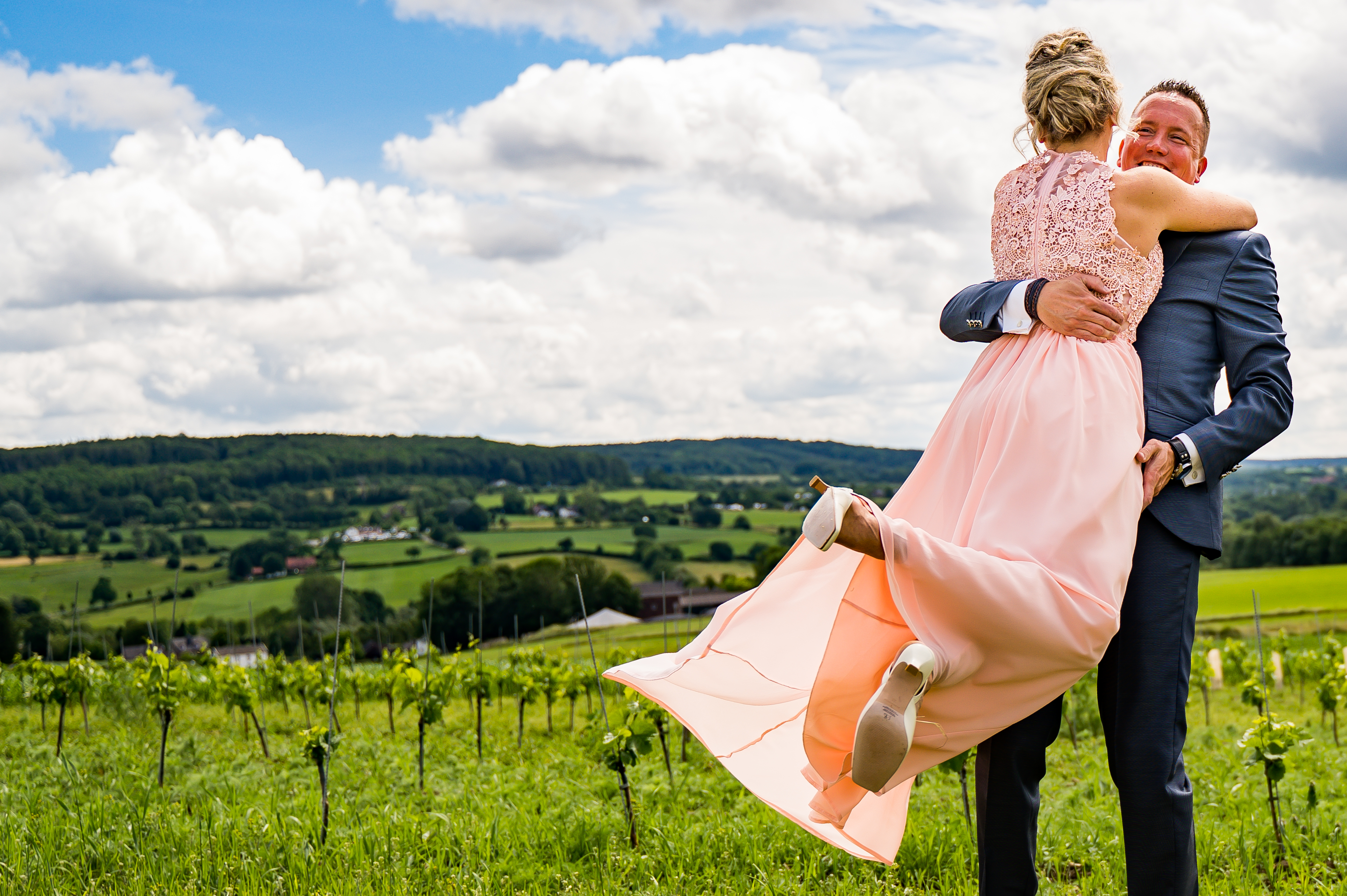 Brautpaar umarmt sich im Weinberg, mit Hügeln im Hintergrund